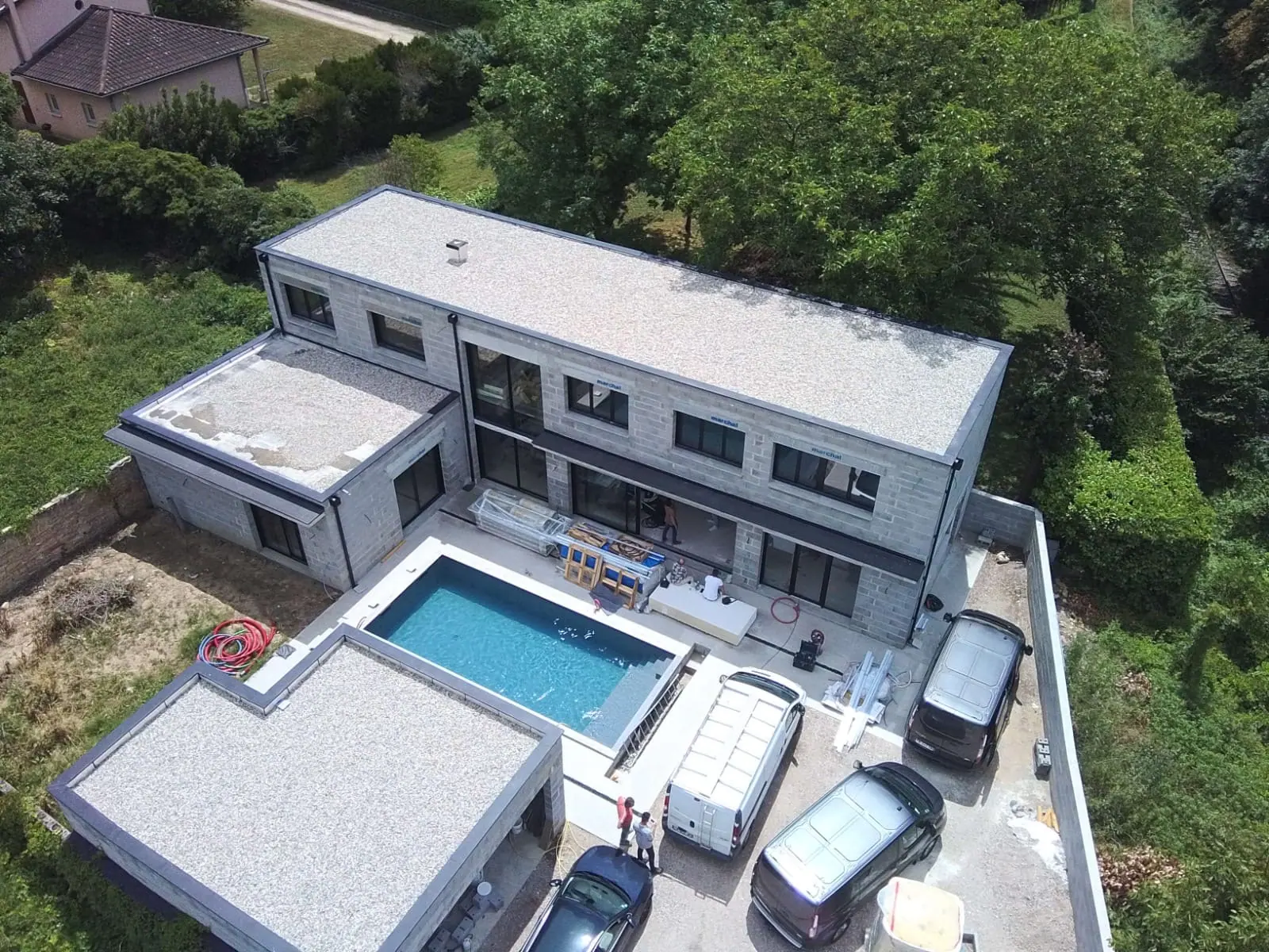 Maison achevée avec bassin béton en premier plan, plages et local technique intégrés au terrain.