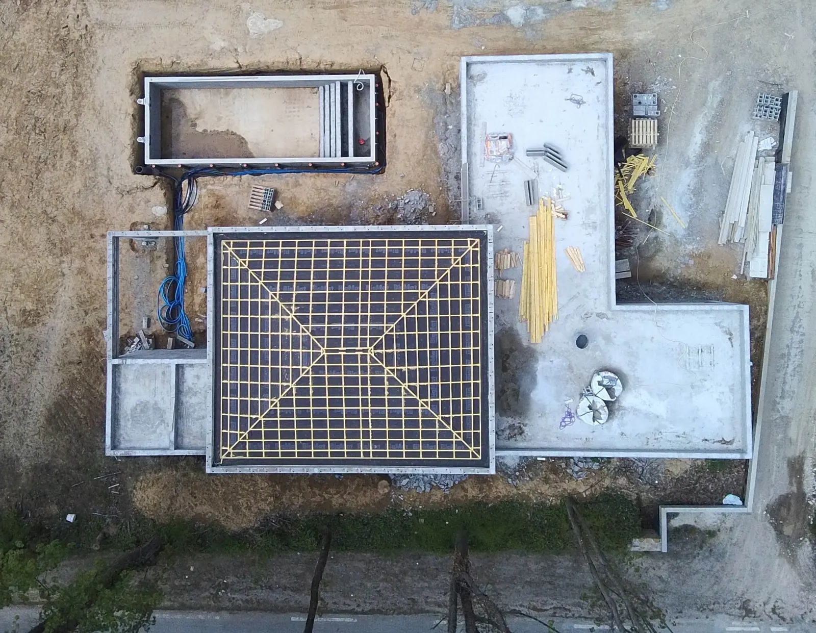 Vue verticale d'un chantier : treillis soudé ligaturé en attente de coulage, murs de soubassement et bassin de piscine coffré.